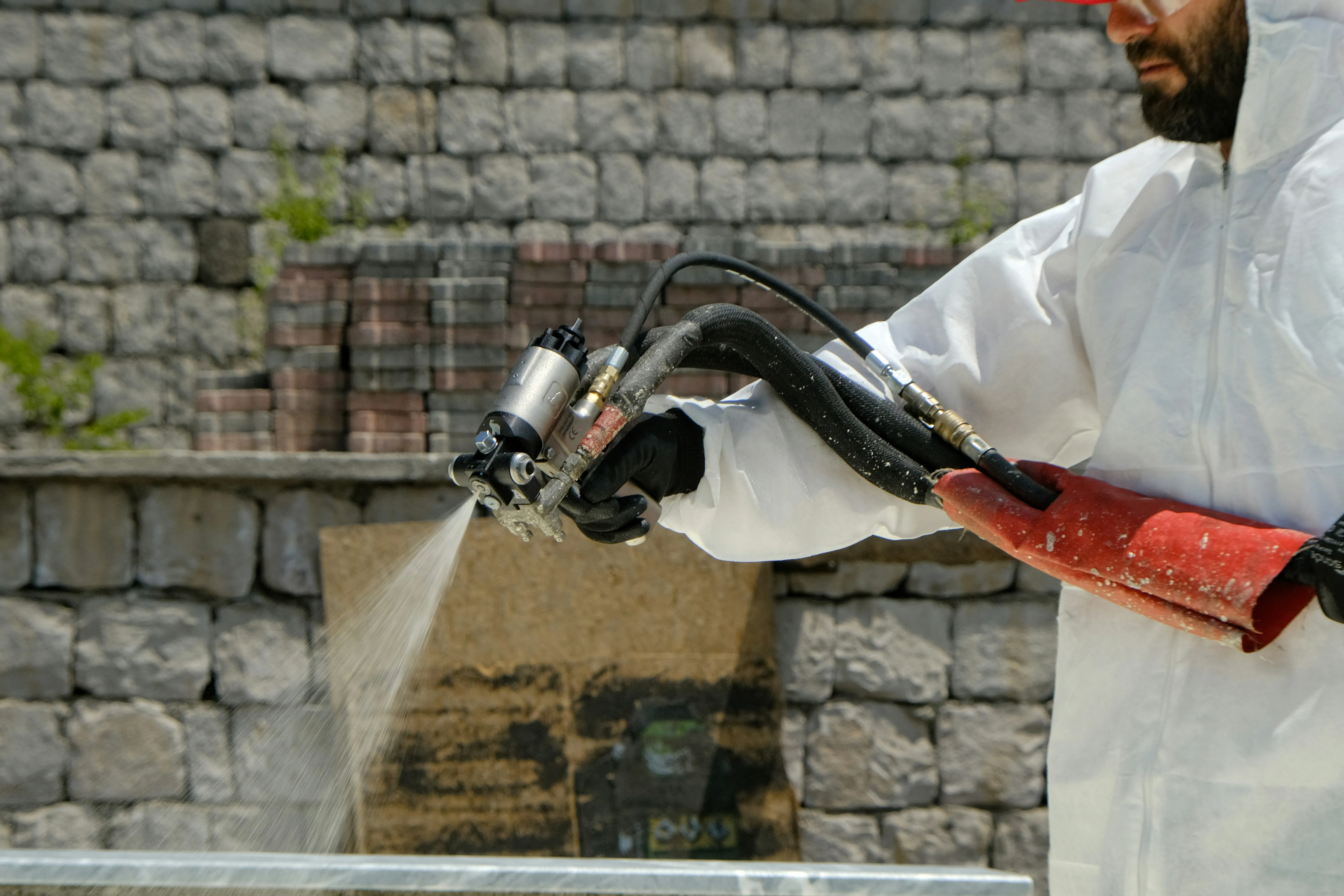 Opérateur en combinaison de protection effectuant un aérogommage sur chantier